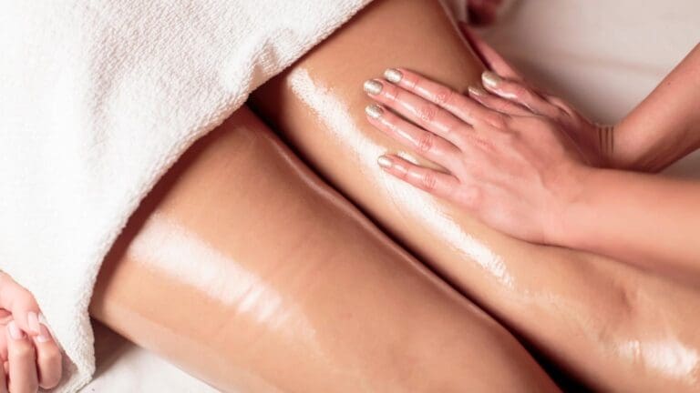 Mano realizando masaje con aceite en piernas femeninas para aliviar la sensación de pesadez y mejorar la circulación.