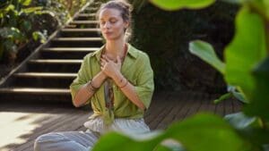 Mujer practicando mindfulness en la naturaleza, sentada en calma con los ojos cerrados, representando meditación guiada, atención plena y reducción del estrés.
