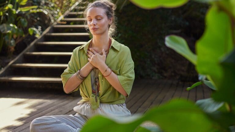 Mujer practicando mindfulness en la naturaleza, sentada en calma con los ojos cerrados, representando meditación guiada, atención plena y reducción del estrés.
