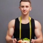 Persona en ropa cómoda haciendo estiramientos suaves en casa junto a una mesa con frutas y verduras, representando el equilibrio entre actividad física y alimentación saludable para reducir el estrés