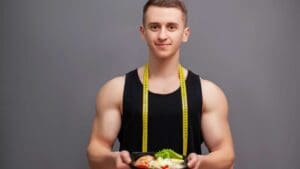 Persona en ropa cómoda haciendo estiramientos suaves en casa junto a una mesa con frutas y verduras, representando el equilibrio entre actividad física y alimentación saludable para reducir el estrés