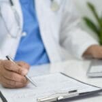 Médico revisando un formulario de contratación junto a un ordenador portátil en un hospital