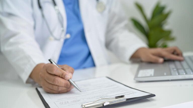 Médico revisando un formulario de contratación junto a un ordenador portátil en un hospital