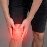 Persona con dolor crónico en la rodilla sujetándola con las manos. Representación de molestias físicas tratadas mediante pedagogía del dolor.