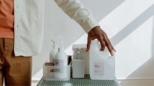 Productos de limpieza sin fosfatos sobre una mesa junto a una persona simbolizando sostenibilidad, cuidado de la piel y del hogar.
