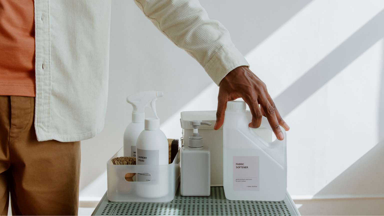 Productos de limpieza sin fosfatos sobre una mesa junto a una persona simbolizando sostenibilidad, cuidado de la piel y del hogar.