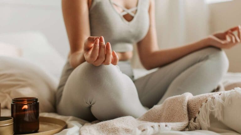 mujer practicando yoga en un espacio sereno con una vela encendida y una manta doblada junto a ella, creando una atmósfera de calma y conexión