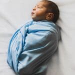 Recién nacido envuelto en manta azul durante sesión de fotos newborn sobre fondo blanco en estudio fotográfico