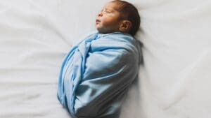 Recién nacido envuelto en manta azul durante sesión de fotos newborn sobre fondo blanco en estudio fotográfico