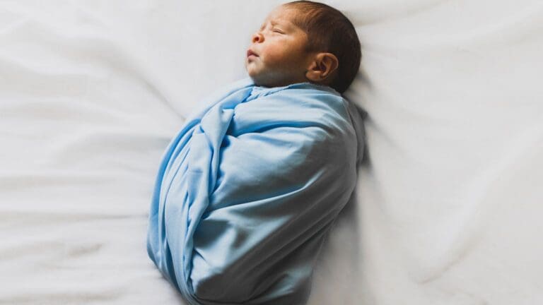Recién nacido envuelto en manta azul durante sesión de fotos newborn sobre fondo blanco en estudio fotográfico