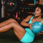 Mujer de más de 40 años entrenando con balón en un gimnasio luminoso, enfocada en su plan de pérdida de peso y hábitos saludables