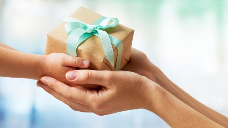 Manos entregando un paquete envuelto con cinta verde pastel que simboliza regalos personalizados llenos de intención y significado.