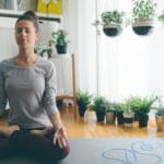 Mujer practicando yoga consciente en casa sobre esterilla con luz natural y ambiente de calma para bienestar físico y mental