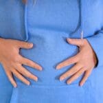 Persona con inflamación abdominal llevándose las manos al estómago. Imagen representativa del malestar que puede abordar una nutricionista.