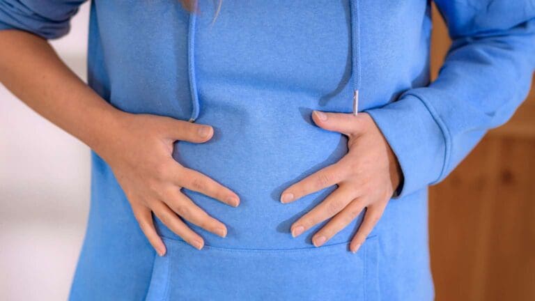 Persona con inflamación abdominal llevándose las manos al estómago. Imagen representativa del malestar que puede abordar una nutricionista.