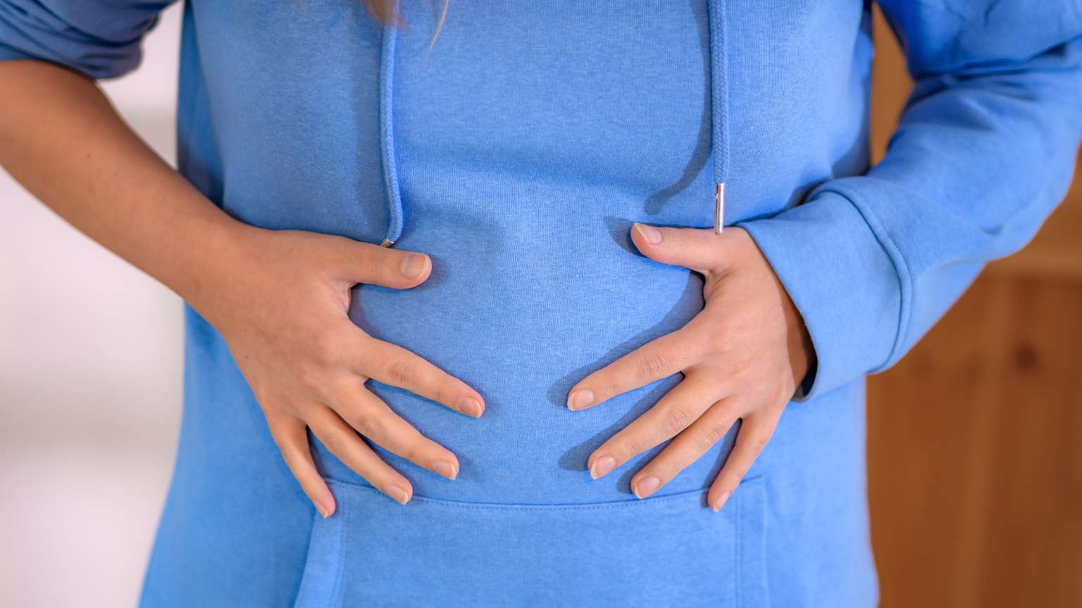 Persona con inflamación abdominal llevándose las manos al estómago. Imagen representativa del malestar que puede abordar una nutricionista.