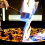 Chef cocinando paella tradicional valenciana al aire libre durante un evento con fuego de leña y paellera gigante