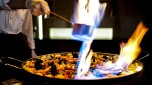 Chef cocinando paella tradicional valenciana al aire libre durante un evento con fuego de leña y paellera gigante