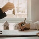 Persona firmando contrato para la compra de vivienda mientras recibe las llaves de una propiedad