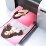 Persona imprimiendo fotos desde el móvil en casa, con copias en papel sobre la mesa.