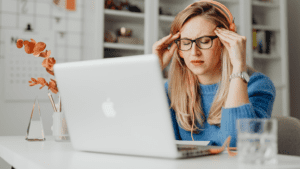 Mujer con dolor de cabeza trabajando frente a un ordenador portátil