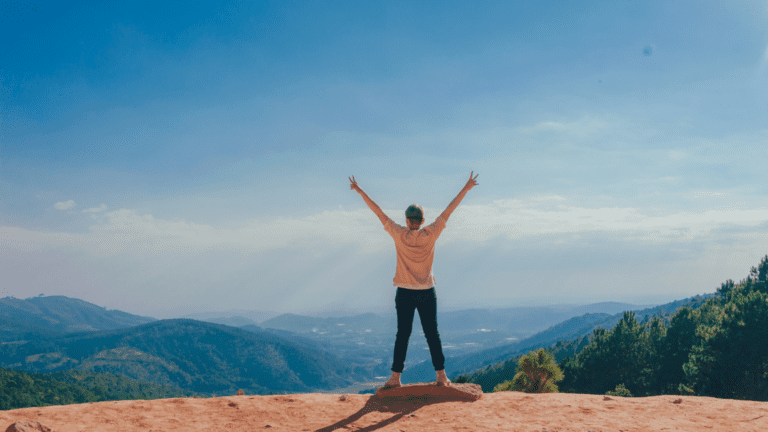 Persona con los brazos en alto disfrutando de la vista en la montaña.