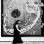 Mujer caminando frente a una obra abstracta en blanco y negro en una galería de arte contemporáneo.