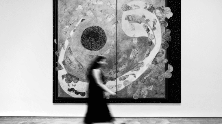 Mujer caminando frente a una obra abstracta en blanco y negro en una galería de arte contemporáneo.