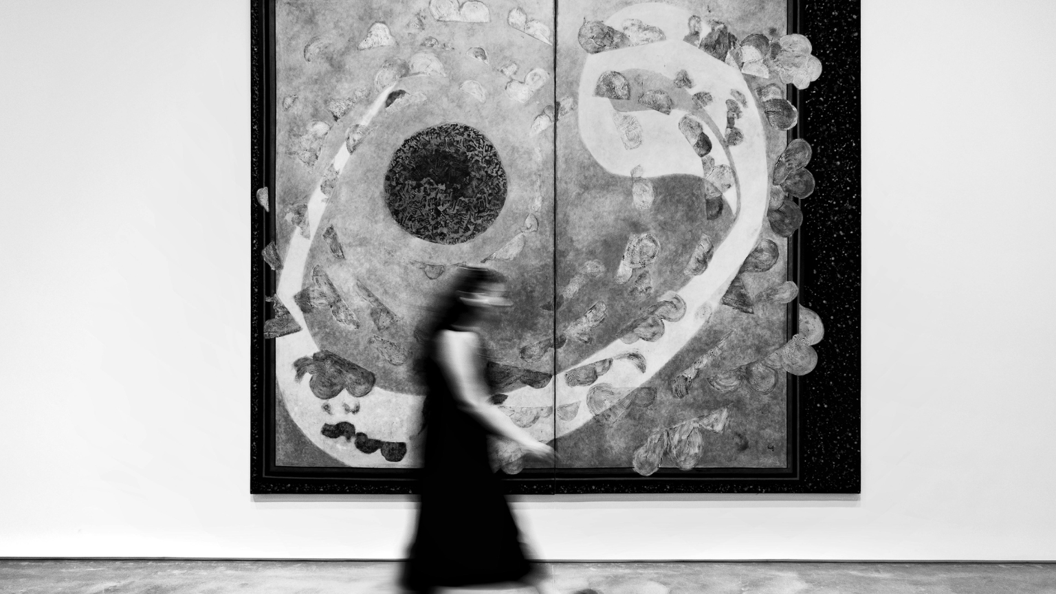Mujer caminando frente a una obra abstracta en blanco y negro en una galería de arte contemporáneo.