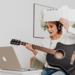 Mujer recibiendo clase de canto online con guitarra y partitura desde casa.