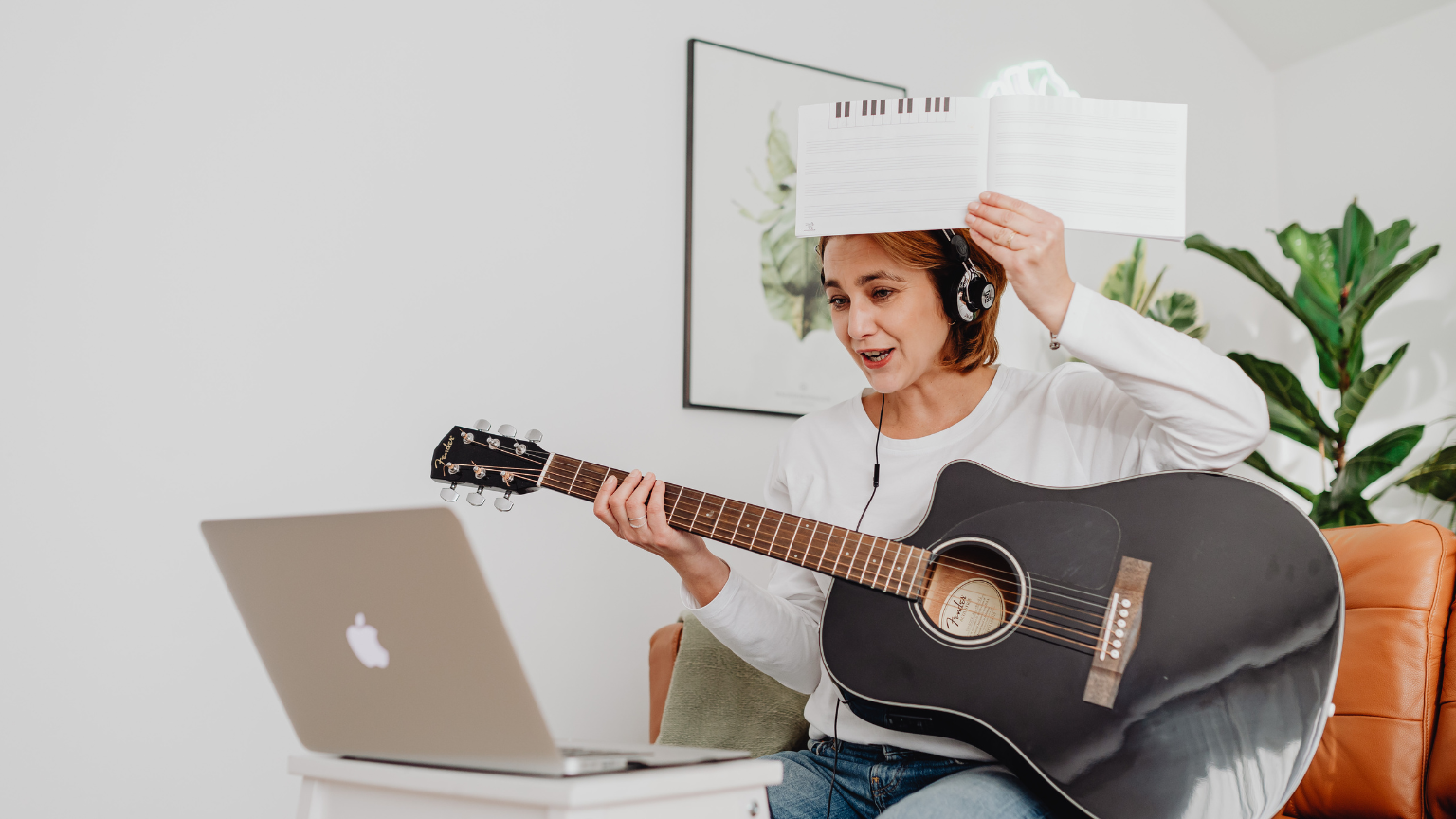 Mujer recibiendo clase de canto online con guitarra y partitura desde casa.