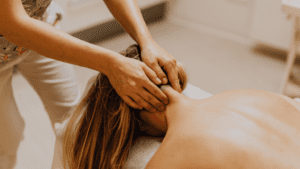 Terapeuta realizando un masaje en la zona cervical de una mujer en camilla dentro de un centro de masajes con ambiente relajante.