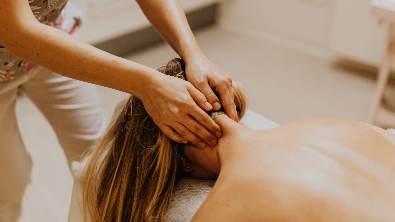 Terapeuta realizando un masaje en la zona cervical de una mujer en camilla dentro de un centro de masajes con ambiente relajante.