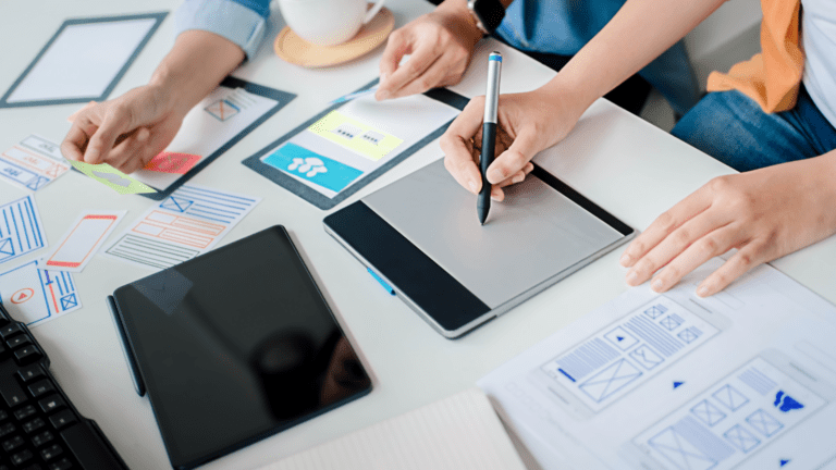 Diseño de interfaz de usuario en equipo creativo con tabletas gráficas y wireframes sobre escritorio.