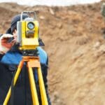 Topógrafo realizando un levantamiento de terreno con estación total.