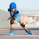 Niño practicando patinaje con protecciones en una escuela de patinaje infantil, desarrollando equilibrio y coordinación al aire libre.