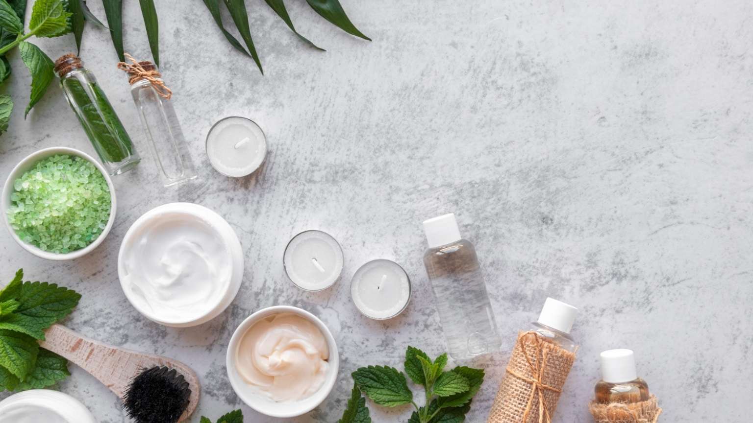 Productos de cosmética natural en envases neutros junto a hojas verdes sobre fondo claro minimalista.