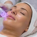 Mujer relajada recibiendo limpieza facial profesional en centro de estética, con piel luminosa y ambiente de bienestar.