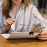 Autónomo revisando documentación en una cafetería moderna, rodeado de papeles y portátil, simbolizando dudas legales sobre licencias de actividad