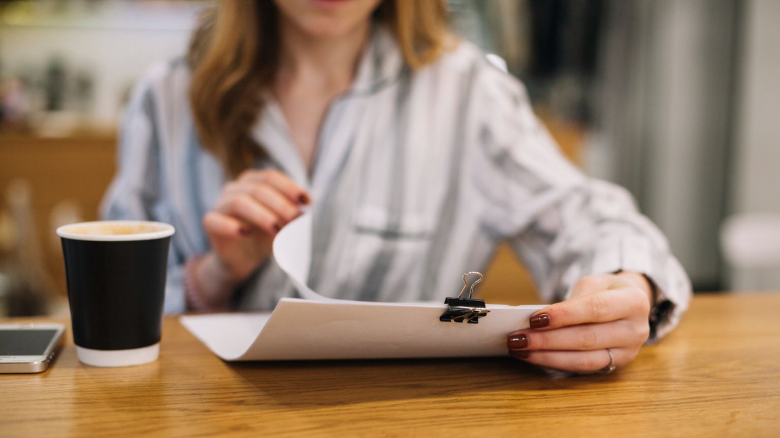 Autónomo revisando documentación en una cafetería moderna, rodeado de papeles y portátil, simbolizando dudas legales sobre licencias de actividad