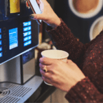 Empleados utilizando máquinas de café vending en una oficina moderna.