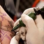 Tattoo artist trabajando con máquina y guantes en un tattoo studio profesional realizando tatuajes con máxima higiene y precisión.