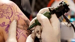 Tattoo artist trabajando con máquina y guantes en un tattoo studio profesional realizando tatuajes con máxima higiene y precisión.