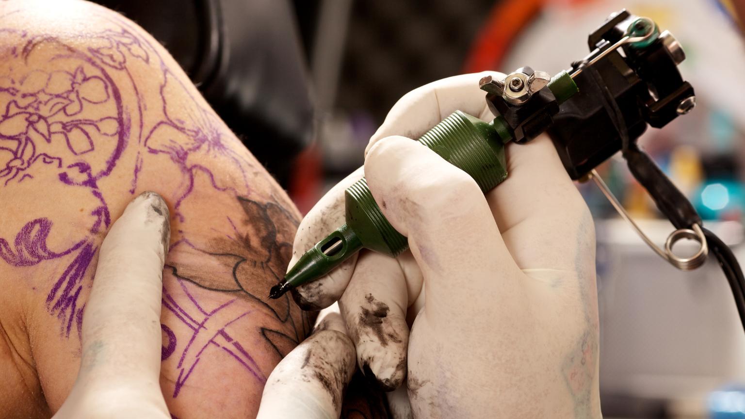 Tattoo artist trabajando con máquina y guantes en un tattoo studio profesional realizando tatuajes con máxima higiene y precisión.