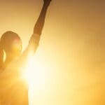 Mujer levantando el brazo al amanecer simbolizando el empoderamiento femenino y el bienestar cotidiano