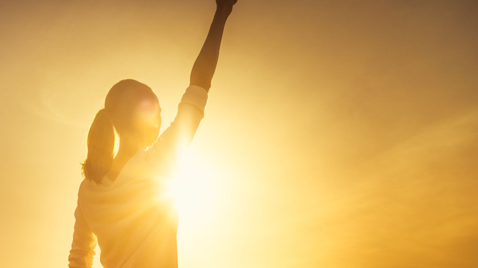 Mujer levantando el brazo al amanecer simbolizando el empoderamiento femenino y el bienestar cotidiano