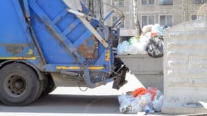 camión de recogida de residuos vaciando contenedor con bolsas de basura acumuladas en zona urbana