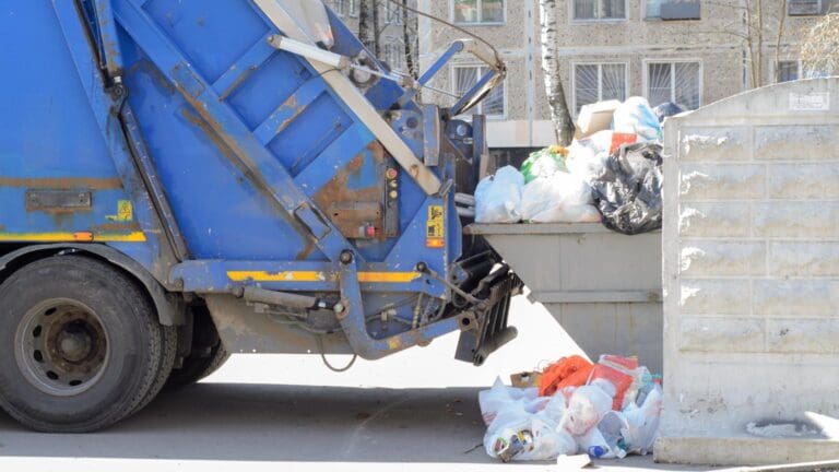 camión de recogida de residuos vaciando contenedor con bolsas de basura acumuladas en zona urbana