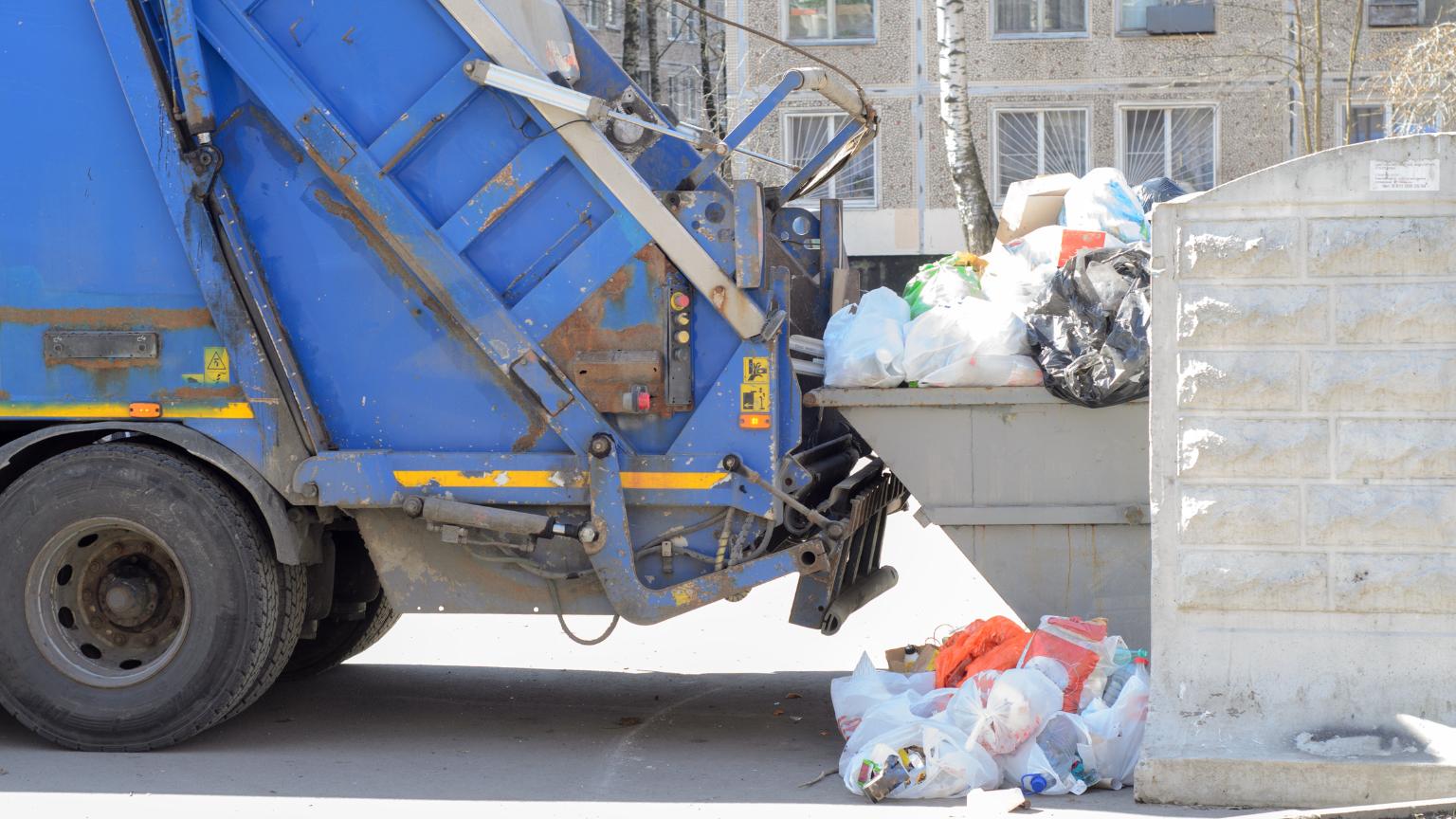 camión de recogida de residuos vaciando contenedor con bolsas de basura acumuladas en zona urbana