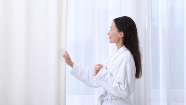 Huésped disfrutando de una vivienda vacacional limpia y luminosa al abrir las cortinas